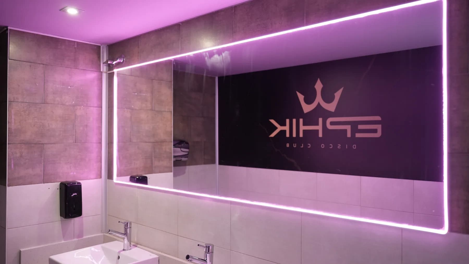 Espejo de los aseos de EPHIK con luz rosa y el logotipo reflejado.